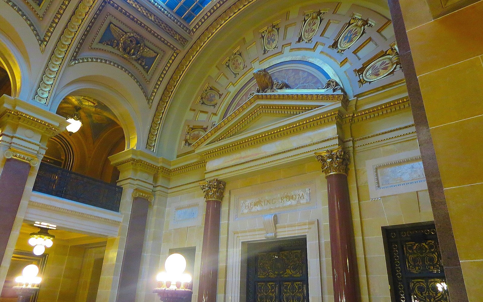 A congressional hearing room photographed from the public gallery, a witness table and microphones visible below, a handful of adult figures seated