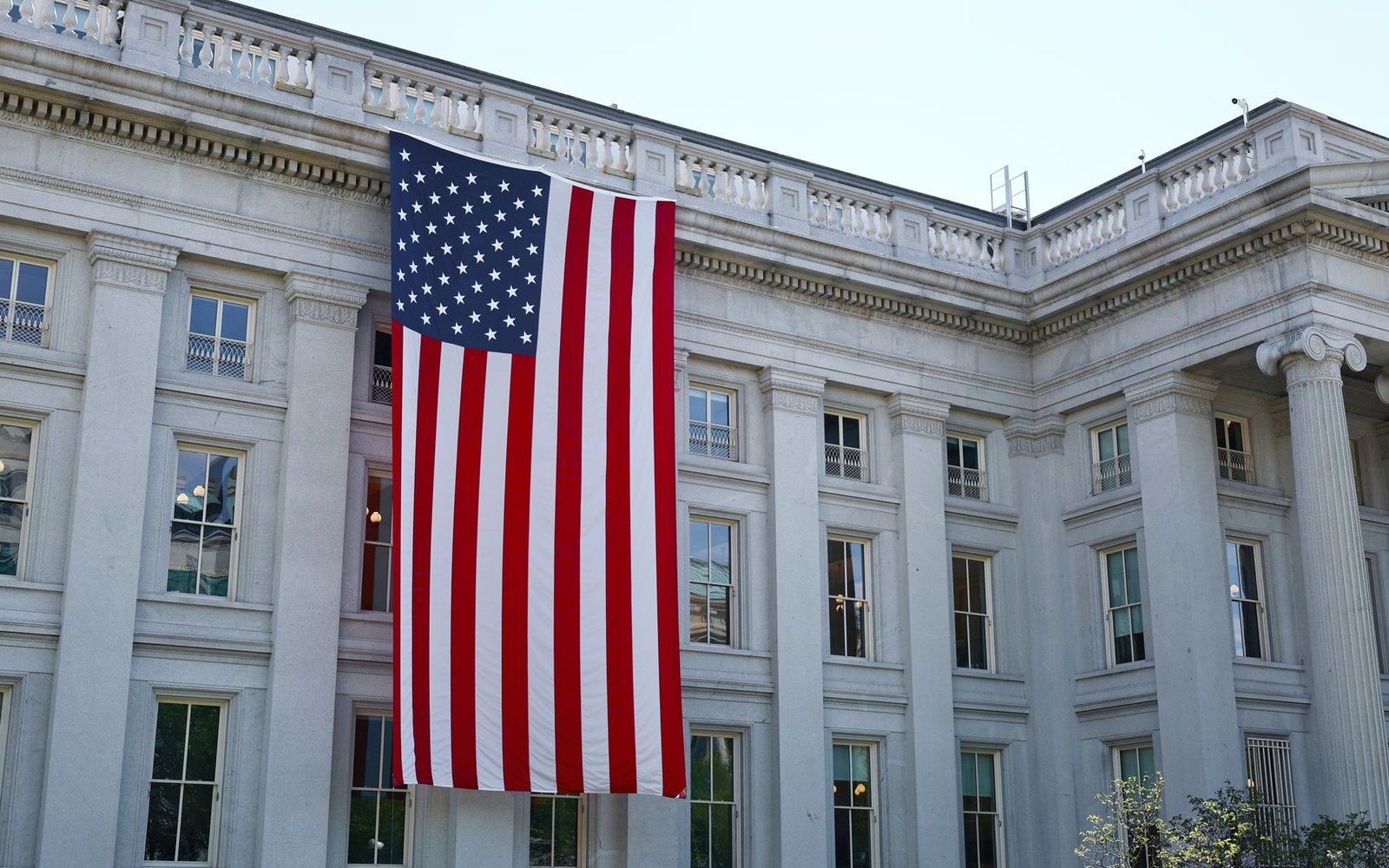 A large American flag hangs vertically on a colonnaded government building facade