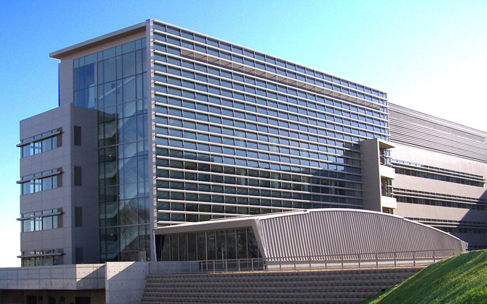 Modern glass and metal office building with a curved canopy entrance under a blue sky