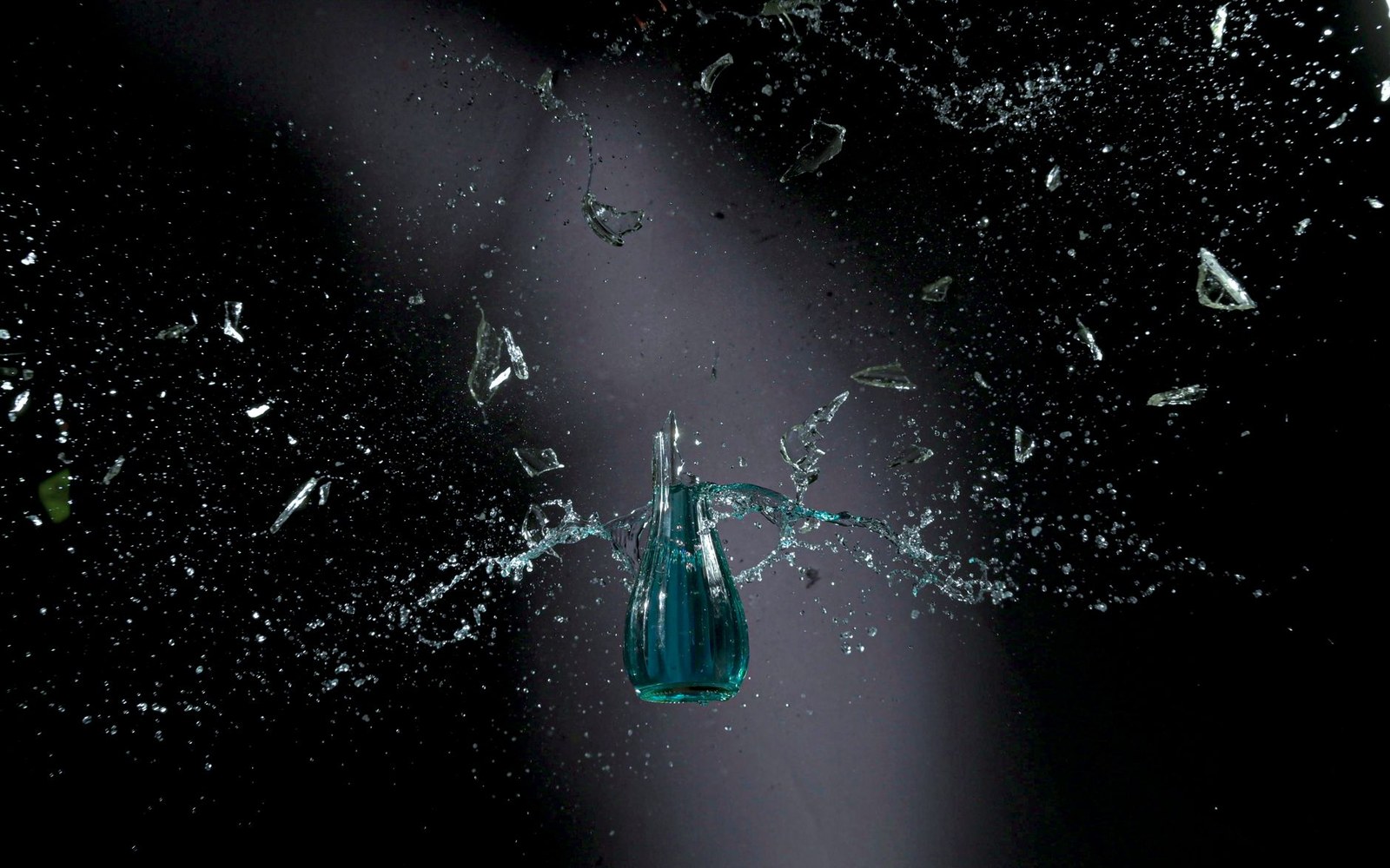 A glass jug shatters into flying shards against a dark background