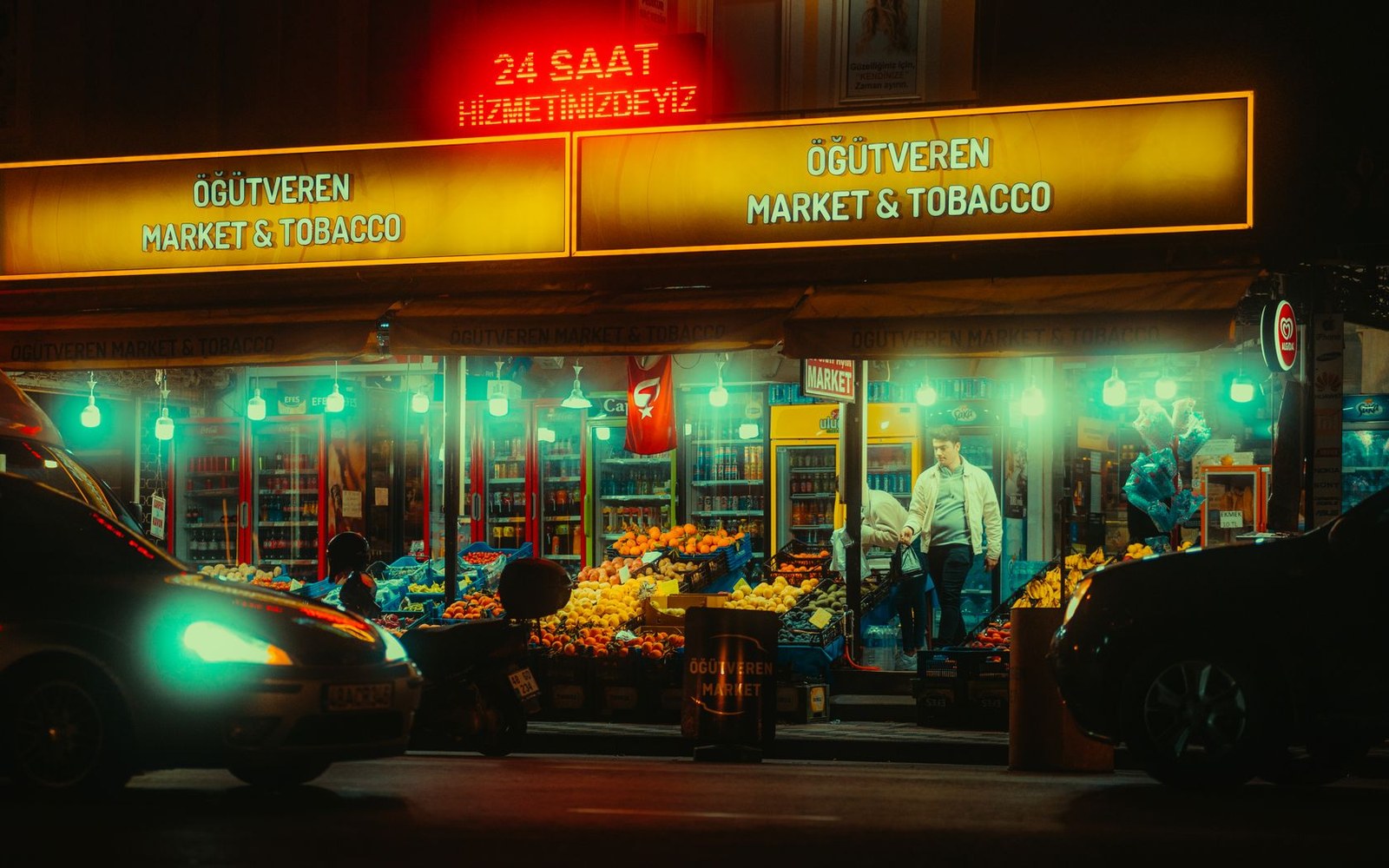 A market and tobacco shop lit up at night with fruit displays out front