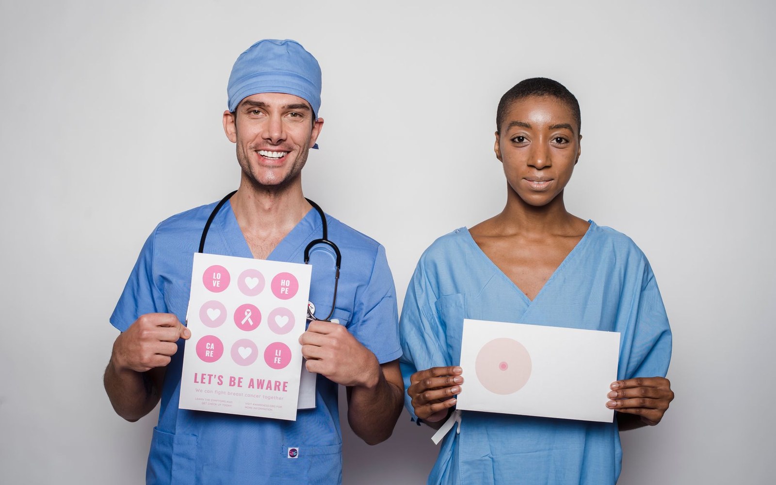 Two medical professionals in scrubs hold breast cancer awareness signs promoting early detection