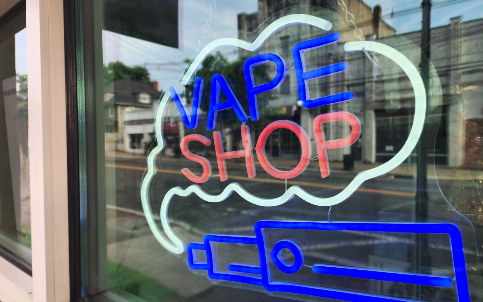 A retail vape display case photographed through its glass front, product rows visible behind the glazing